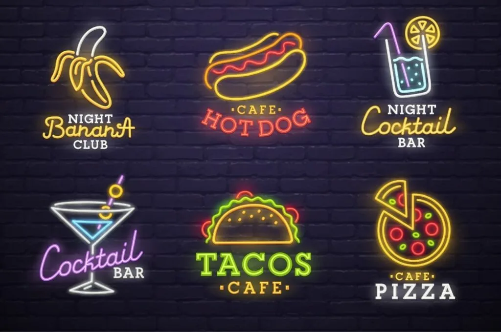 Colorful neon signs illuminate a street, advertising various restaurants and bars in a vibrant nightlife setting.